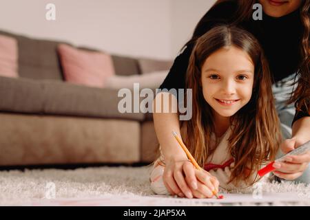 Piccola ragazza bionda graziosa sorridente insieme con la sua madre nel paese che attira sul papre usando la matita rossa, concetto del tempo della famiglia insieme. Foto Stock