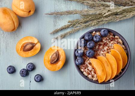 Colazione sana. Fiocchi d'avena a grani interi con fette di albicocca e mirtilli su un tavolo di legno dipinto di blu Foto Stock