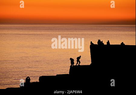 Forme di persone sedenti e in piedi su un groyne a Brighton Beach, dopo aver guardato il tramonto. Il cielo aglow con la luce fadign del giorno. Brighton, Inghilterra, Regno Unito Foto Stock