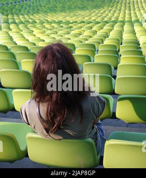 Da sola giovane donna sul sedile nel bleache dello stadio e molti posti liberi Foto Stock