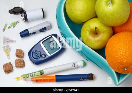 Glucometro, penna per siringa per insulina, vaso di zucchero con mele e arance su tavola bianca. Concetto di nutrizione diabetica Foto Stock