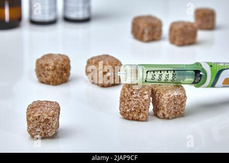 Una goccia di insulina sulla punta dell'ago e zucchero di canna sparso su sfondo bianco. Giorno del diabete Foto Stock