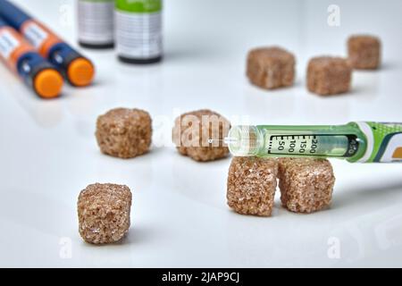 Una goccia di insulina sulla punta dell'ago e zucchero di canna sparso sullo sfondo di una penna per siringa. Giorno del diabete Foto Stock