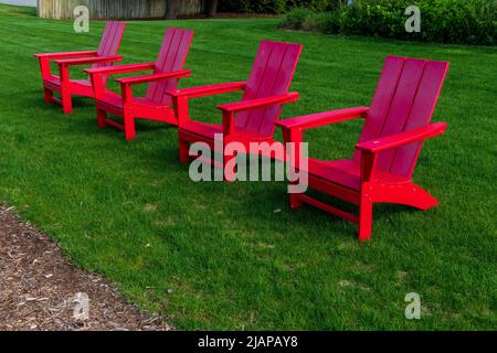 Fila di sedie rosse Adirondack sulla riva del lago su un prato erboso Foto Stock
