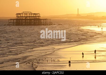 Forme di persone sulla spiaggia a bassa marea, Brighton & Hove, East Sussex, Inghilterra, Regno Unito. Resti del West Pier e della centrale elettrica di Shoreham in lontananza. Foto Stock