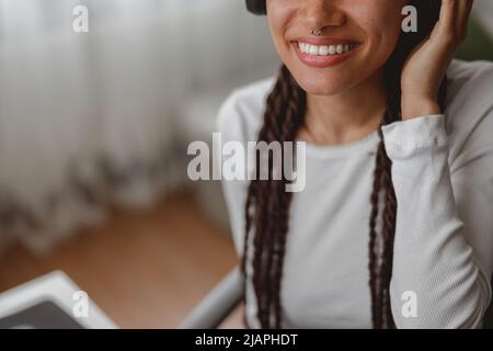 Primo piano di una bella donna gioiosa indossando cuffie con piercing in naso che sorride al chiuso Foto Stock