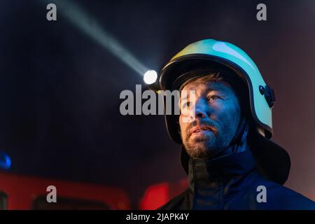 Primo piano di un pompiere con camion dei pompieri in background di notte. Foto Stock