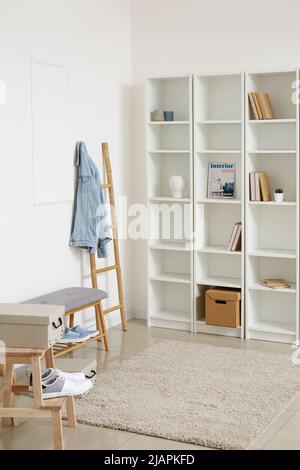 Elegante scaffale e morbida panca con scarpe vicino alla parete bianca Foto Stock