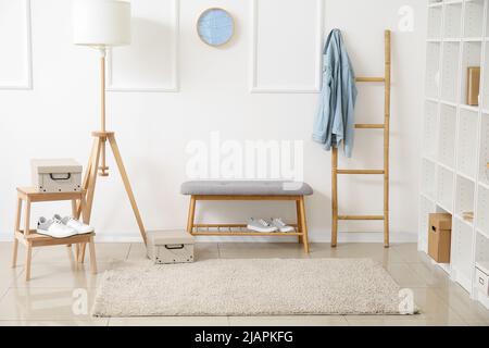 Comodo pouf, lampada moderna e scala vicino alla parete bianca Foto Stock