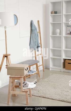 Elegante scaffale e morbida panca con scarpe vicino alla parete bianca Foto Stock