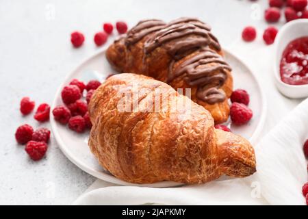 Piatto di deliziosi croissant con lamponi su sfondo chiaro Foto Stock