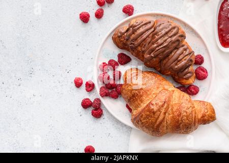 Piatto di deliziosi croissant con lamponi su sfondo chiaro Foto Stock