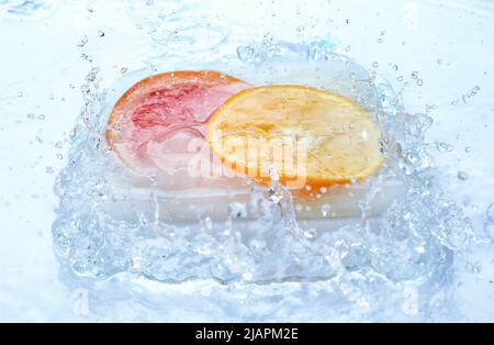 Fette fresche di agrumi surgelati con acqua spruzzata su sfondo bianco Foto Stock