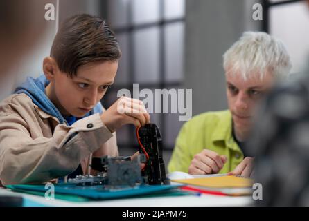 Insegnante che lavora insieme ai bambini su progetto con giocattoli elettrici e robot in classe robotica, aiutandoli Foto Stock