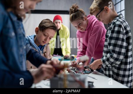 Gruppo di ragazzi che lavorano insieme a progetti con giocattoli elettrici e robot in aula di robotica Foto Stock