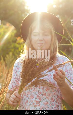 Sfocare primo piano ritratto esterno di bella giovane bionda donna su sfondo natura. Donna che tiene mazzo di pampas erba. Salute mentale, all'aperto. Li Foto Stock