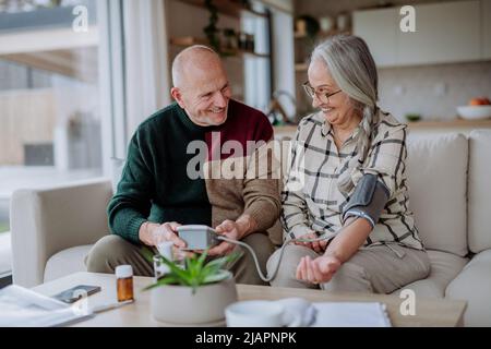 Coppia anziana a casa che misura la pressione sanguigna. Foto Stock