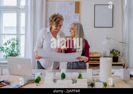 Le donne mature eco architetti con modello di moderni bulidings e progetti che lavorano insieme in ufficio. Foto Stock