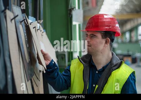 Giovane uomo con sindrome Down che lavora in fabbrica industriale, concetto di integrazione sociale. Foto Stock