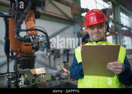 Giovane uomo con sindrome Down che lavora in fabbrica industriale, concetto di integrazione sociale. Foto Stock