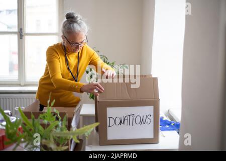 Donna volontaria senior che confezionano una scatola con aiuti umanitari per i rifugiati ucraini in carica Foto Stock