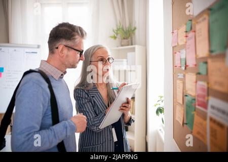 Dipendente dell'agenzia di reclutamento che si trova di fronte alla bacheca del lavoro e aiuta l'uomo maturo a cercare un lavoro. Foto Stock
