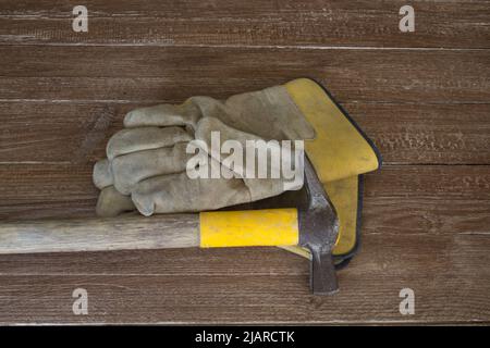 Immagine di un paio di guanti da lavoro e di un martello da muratore. Rappresentazione del lavoro pesante e delle sue possibili lesioni Foto Stock