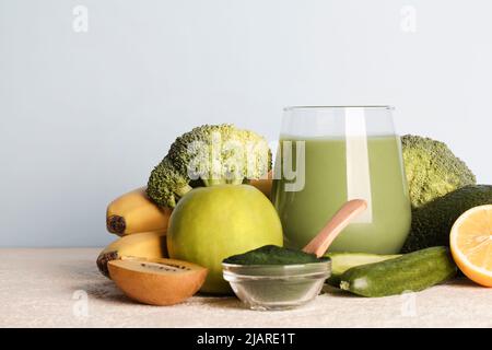 frullato verde in vetro, polvere di spirulina, verdure e frutta su sfondo blu. dieta vegana sana, cruda. spazio copia Foto Stock