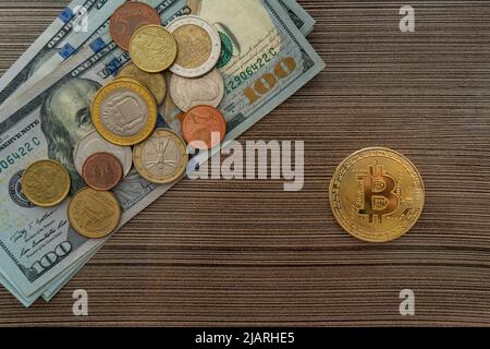 Vista dall'alto di un bitcoin che giace accanto ad una pila di dollari e monete sul tavolo. Investire in valuta o criptovaluta è la scelta del futuro. Foto Stock