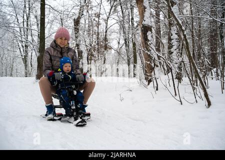 Madre con un bambino su una slitta. Una giovane donna con il suo figlio scivola giù per la collina in una slitta. Famiglia vacanza invernale. Foto Stock