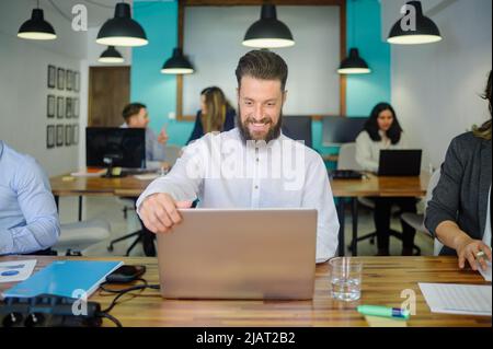 Uomo allegro che lavora su un notebook nello spazio di lavoro Foto Stock