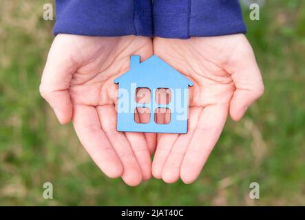 Vista dall'alto di una casa in legno a forma piatta dipinta di blu posta in mani all'aperto. Foto Stock