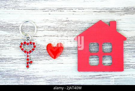 Chiave a scheletro decorata con rhinestones, portachiavi a forma di casa rossa e un piccolo cuore su uno sfondo di legno. Concetto di movimento creativo in Together. Foto Stock
