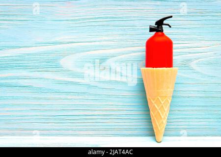 Estintore rosso in miniatura in un cono a cialde su sfondo di legno. Concetto creativo e caldo d'estate. Foto Stock