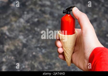 Mano che tiene un cono waffle con un estintore rosso in miniatura su uno sfondo sfocato con spazio copia. Stare al fresco con il tempo caldo. Foto Stock