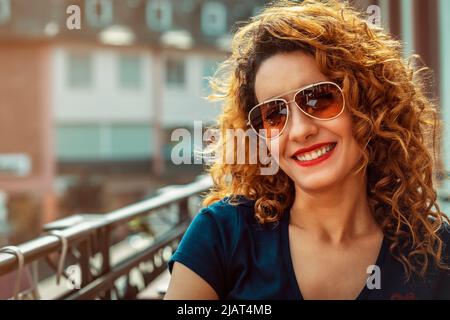 Giovane donna marocchina, con capelli marroni ricci, seduta in un bar all'aperto a Mainz, con occhiali da sole Foto Stock