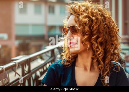 Giovane donna marocchina, con capelli marroni ricci, seduta in un bar all'aperto a Mainz, con occhiali da sole Foto Stock