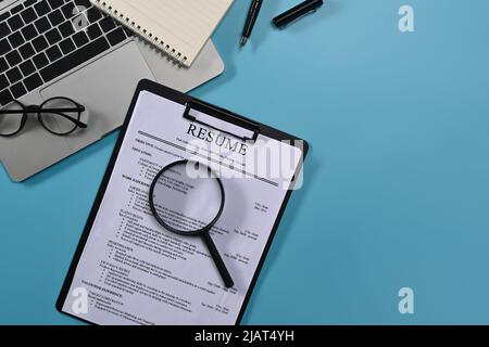 Vista dall'alto computer portatile, lente d'ingrandimento e riassume candidati su sfondo blu. Concetto di ricerca di lavoro Foto Stock