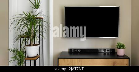 smart tv mockup appeso a parete beige in interni moderni con piante verdi. schermo vuoto Foto Stock