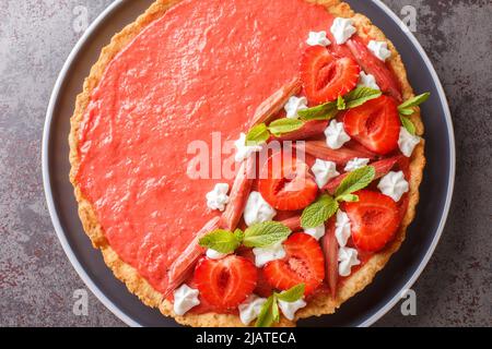 Torta estiva con fragole, rabarbaro, menta e panna montata da vicino su un piatto sul tavolo. Vista dall'alto orizzontale Foto Stock