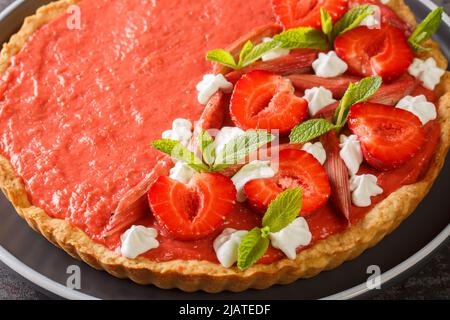 Deliziosa crostata di fragole, rabarbaro, menta e panna montata da vicino su un piatto sul tavolo. Orizzontale Foto Stock