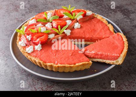 Crostata di fragole e rabarbaro a fette decorata con menta e panna montata primo piano su un piatto sul tavolo. Orizzontale Foto Stock