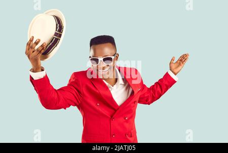 L'uomo africano in abito funky rosso toglie il suo cappello, sorride, fa un arco e vi accoglie a festa Foto Stock