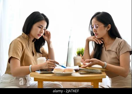 Due studenti universitari femminili millenari stavano facendo i compiti insieme nella caffetteria, Un'amica femminile sta insegnando la sua migliore amica in matematica. Foto Stock