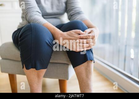 Donna anziana a casa che tiene il suo ginocchio doloroso Foto Stock