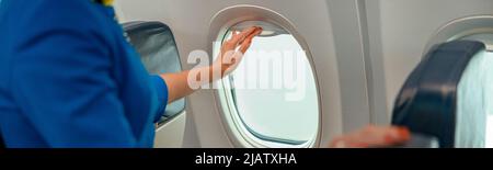 Donna assistente di volo chiusura finestra in aereo Foto Stock