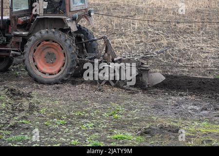 il trattore agricolo con aratro arpa il campo e si prepara alla semina. Foto Stock