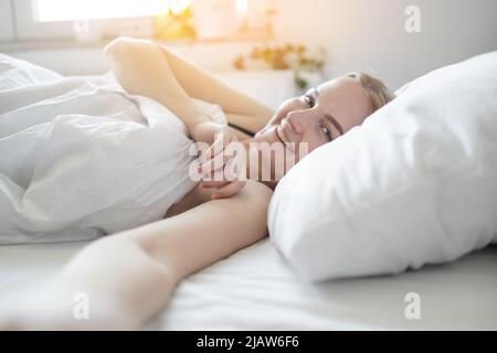 Rilassante giovane sorriso bionda capelli ragazza che rimane nel suo letto al mattino il fine settimana Foto Stock