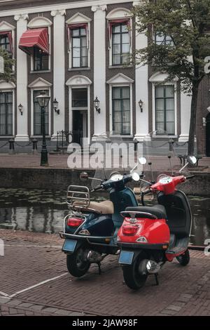 Leiden, Paesi Bassi - 25 luglio 2021: Scooter bianco e blu parcheggiato a Leiden lungo il Vecchio Reno con un canale, con una bella casa sul retro Foto Stock