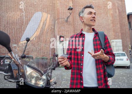Uomo in una camicia rossa a quadri in piedi vicino alla strada motobike Foto Stock